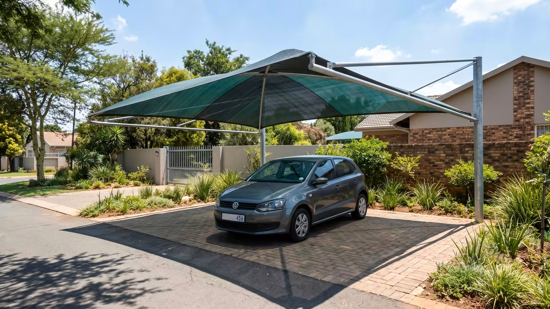 Shade-net shadeport with a green shade-cloth roof covering a car on a suburban driveway